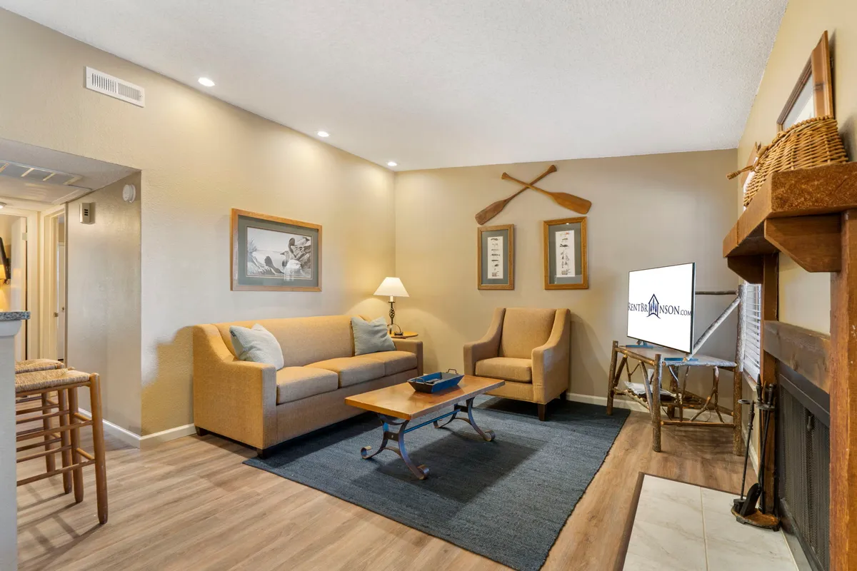 The image features a warm and inviting living room with a plush sofa, cozy chairs, a stylish coffee table, soft lighting from a lamp, tasteful artwork, and a television. This comfortable space is perfect for relaxing, socializing, and enjoying movie nights after a day at Table Rock Lake.