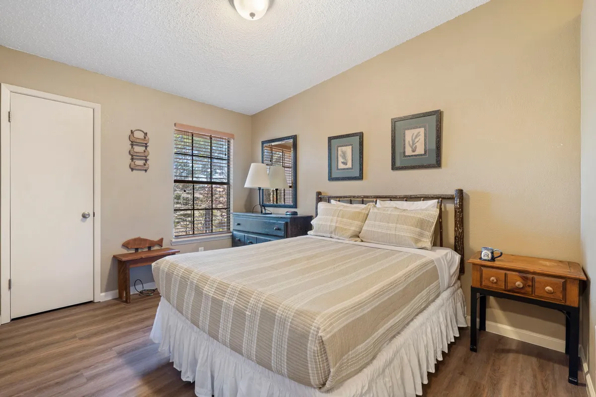 A cozy queen bedroom with a plush bed, decorative frames above the headboard, a nightstand with a lamp, and a window letting in soft, natural light. The room exudes a peaceful, personal retreat vibe, perfect for restful nights.