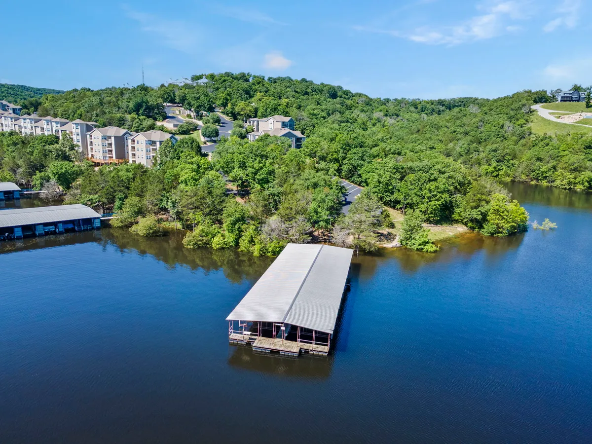 A scenic lakeside view with a dock stretching over tranquil waters, surrounded by greenery and residential buildings, suggesting opportunities for boating, fishing, and lakeside picnics.