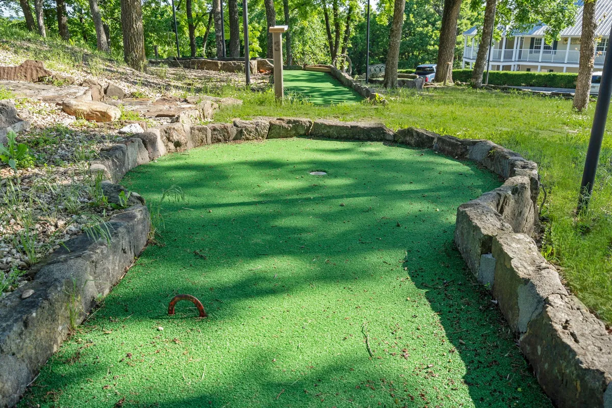 A vibrant outdoor mini-golf course bordered by green carpet and natural stone, inviting families and groups to engage in friendly competition surrounded by lush greenery.