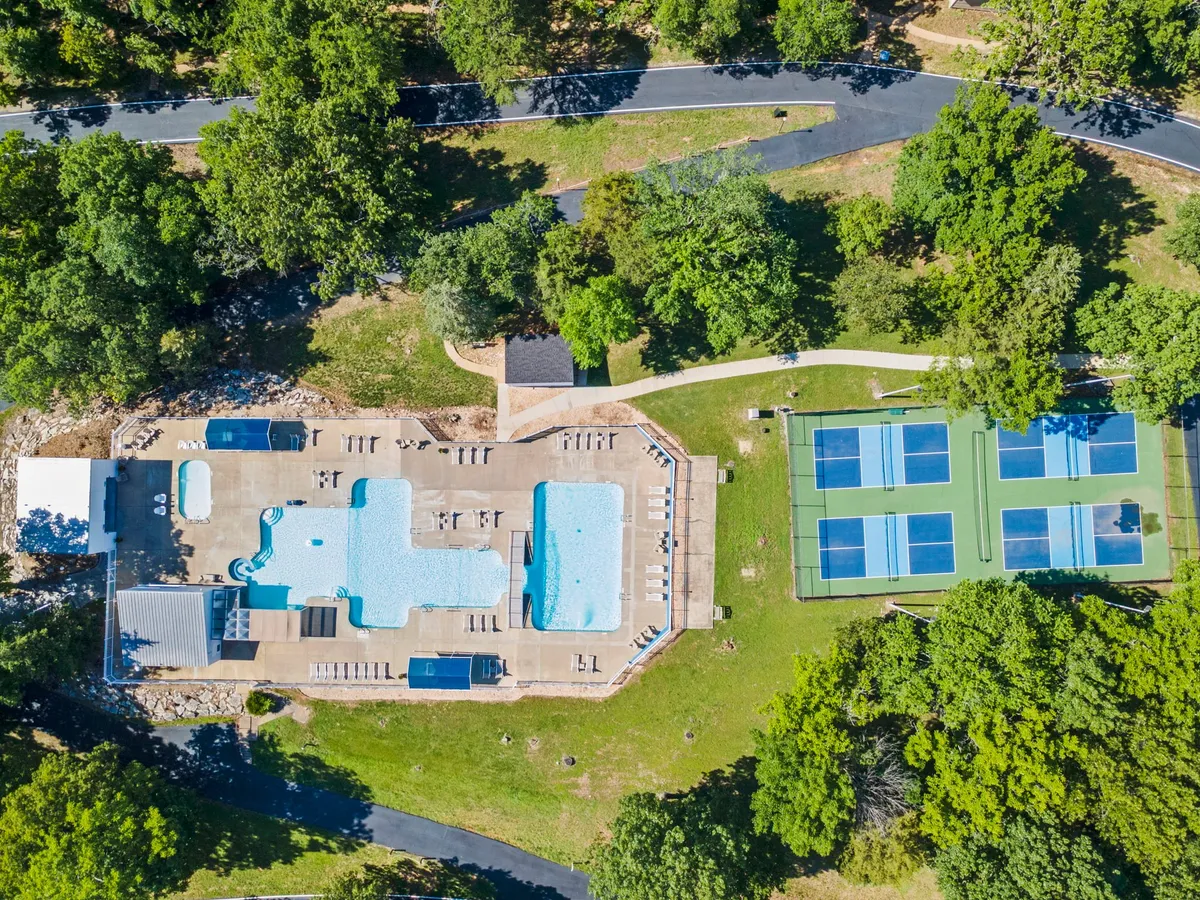 An active, vibrant exterior scene featuring a swimming pool and tennis courts set among lush greenery. The pool area is perfect for sunbathing and social gatherings, while the courts invite friendly matches and outdoor play.