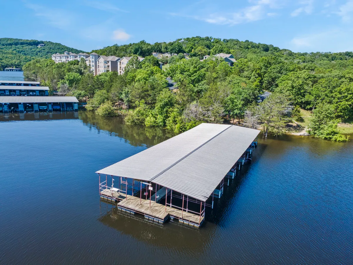 A tranquil lakeside dock extends over calm water, surrounded by lush greenery and with resort buildings visible in the distance. The scene invites activities like fishing, boating, or simply soaking in the view after an active day.