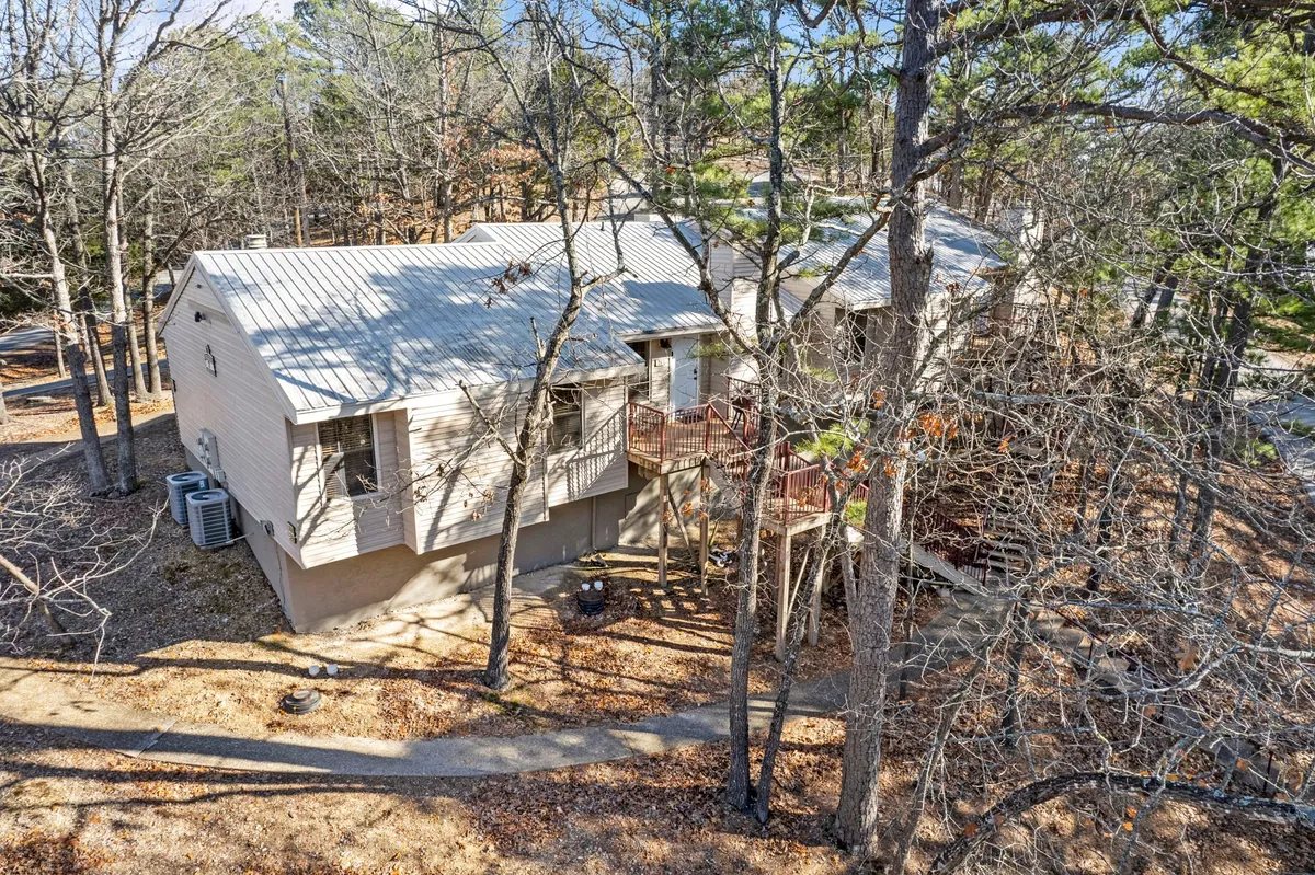A rustic house with a spacious deck nestled among tall trees, offering a tranquil and secluded setting. The deck is surrounded by lush greenery, creating an inviting space to relax and enjoy nature. The elevated vantage point hints at scenic views, ideal for couples seeking privacy and a peaceful retreat.