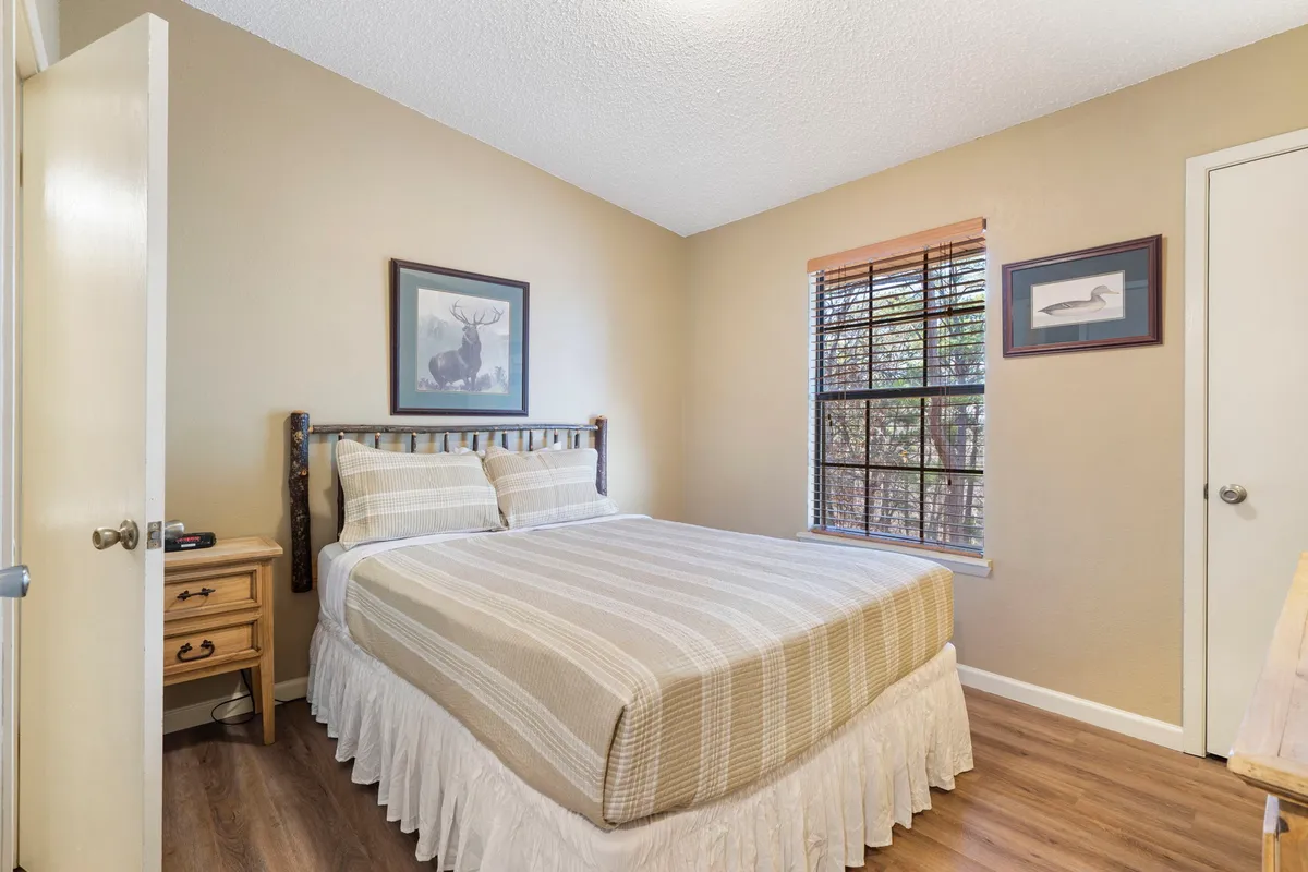 A serene bedroom featuring a neatly made queen bed, framed artwork, a window with sunlight filtering in, and a wooden dresser. The space looks inviting, quiet, and ideal for winding down after a busy day.