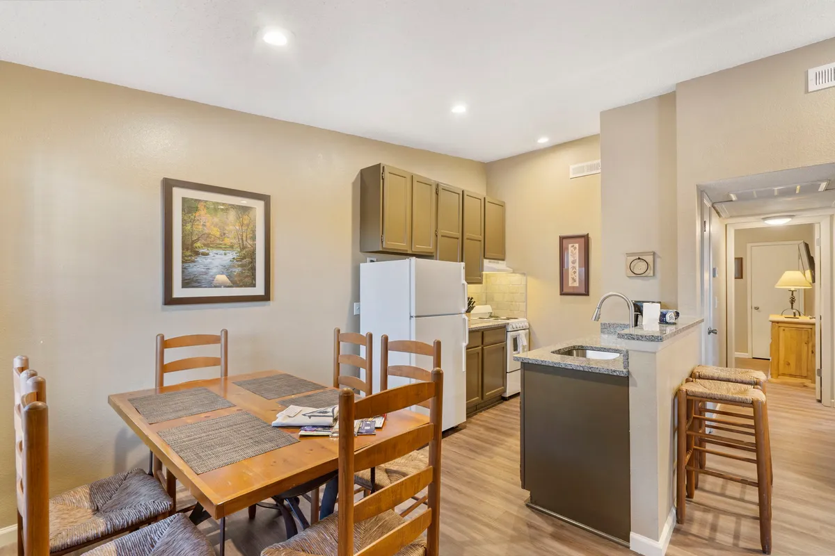A warm, inviting kitchen and dining area with a wooden table set for family meals and modern appliances visible in the background. Framed artwork and soft lighting create a cozy, homely atmosphere, perfect for gathering and celebrating special occasions.