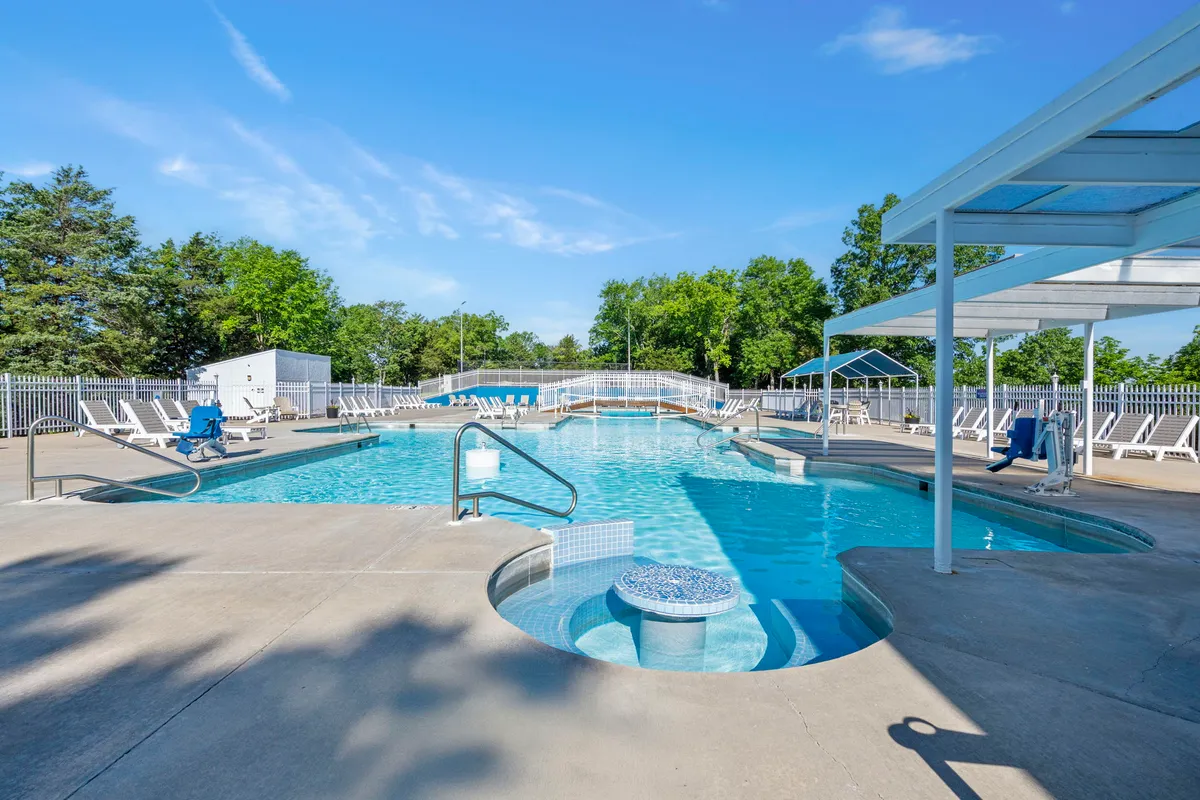 A sparkling swimming pool with a jacuzzi, surrounded by lounge chairs and lush greenery, sets the scene for leisure and socializing on sunny days.
