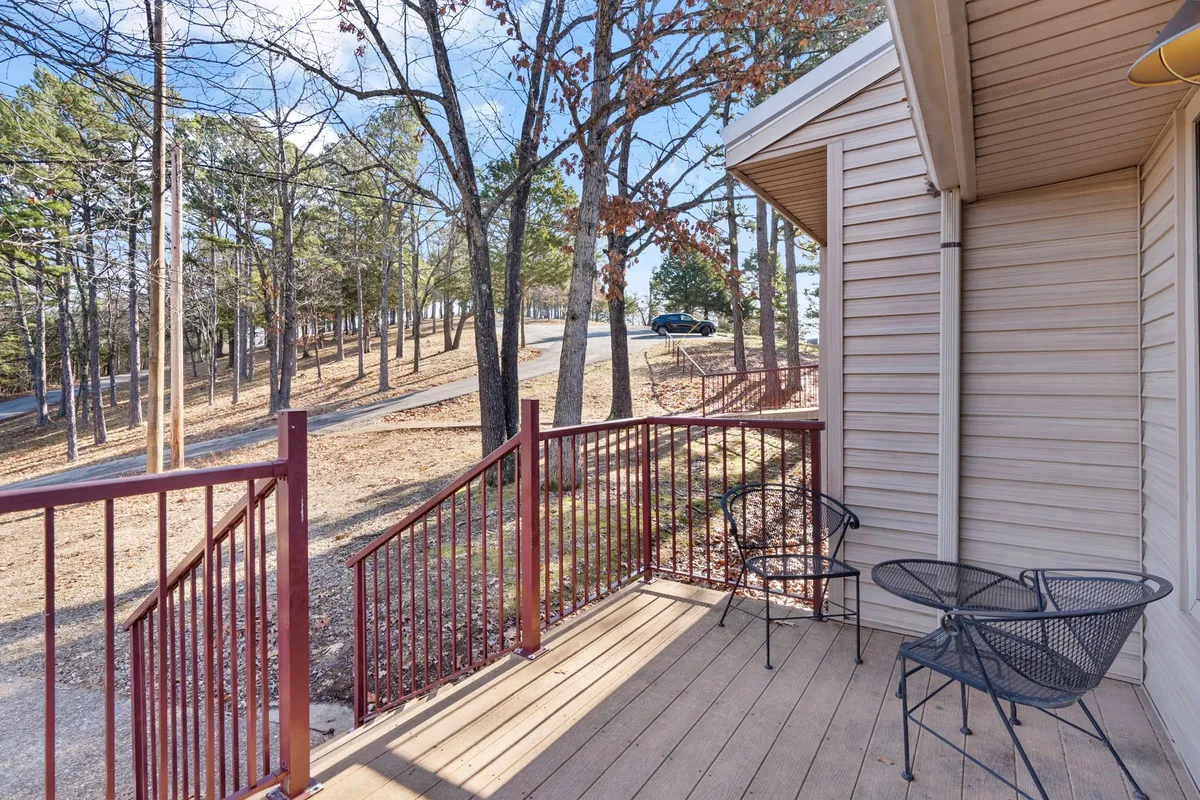 A private wooden deck featuring metal railings and outdoor chairs, surrounded by lush trees. The seating arrangement is inviting, capturing the tranquil atmosphere of an outdoor haven that encourages relaxation while being close to nature.