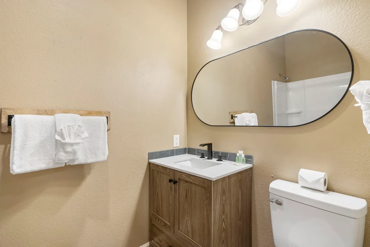 An inviting ensuite bathroom with an oval mirror, a vanity sink, a wooden towel rack, and tasteful light fixtures. The setup is perfect for personal grooming and relaxation, highlighting the private bathroom feature.