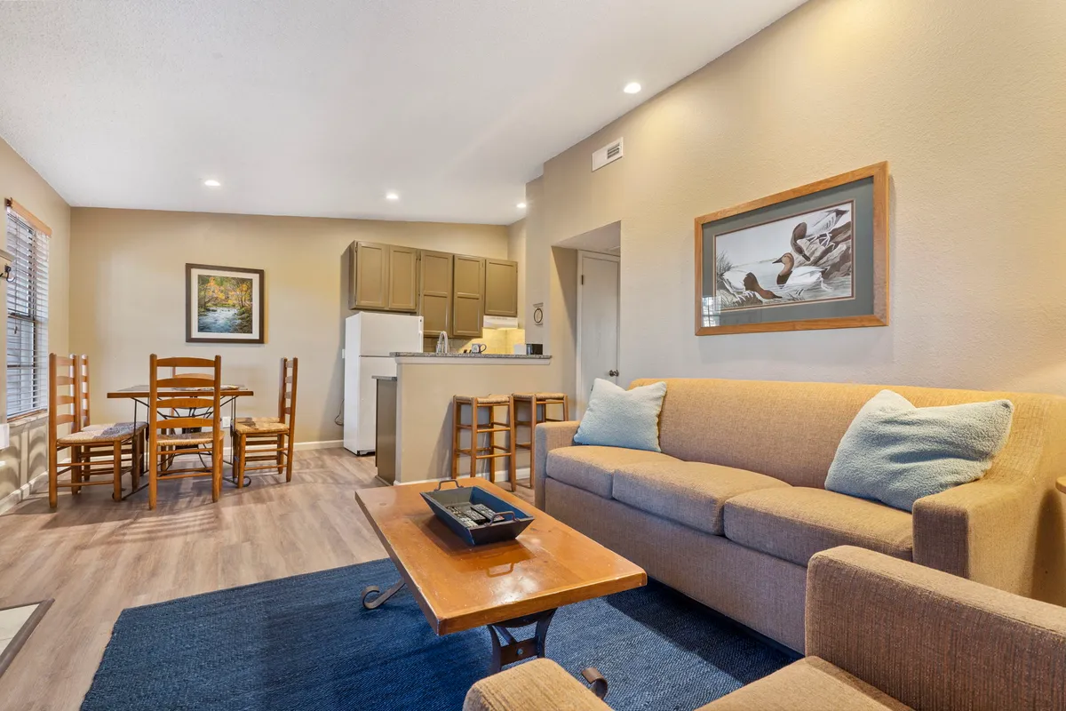 An open-plan interior featuring a plush sofa, a dining table set for meals, and a view into the modern kitchen area. Framed artwork adds personality, while the space feels both comfortable and functional, ideal for relaxing, dining, and socializing after a day of activities.