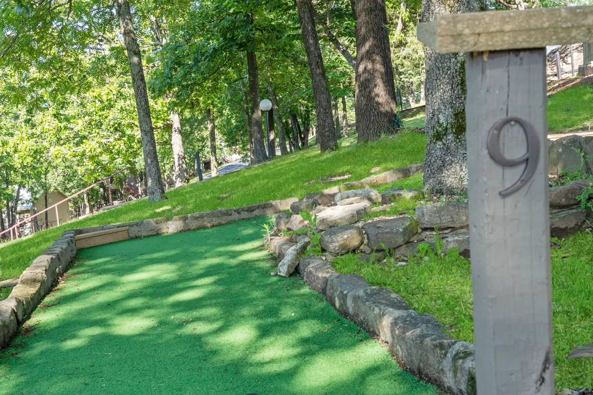 A playful outdoor scene of a green mini-golf putting area bordered by natural landscaping. The space feels inviting and fun, encouraging friendly group competitions and shared outdoor moments.